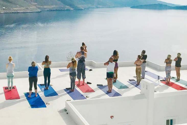 A small group of women practising yoga on a white rooftop terrace above the sea, Amorgos, Greece